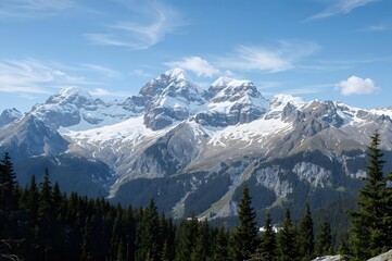 Obraz premium Majestic Mountain Peak under blue sky: Capturing a breathtaking scene of snow-capped mountain peaks against a vivid blue sky, with patches of verdant evergreen forest in the foreground.