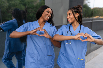 Two smiling multiracial female doctors making heart shape with hands
