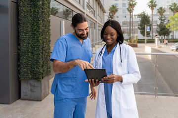 Smiling diverse multiracial doctors discussing patient information using a tablet outside a hospital