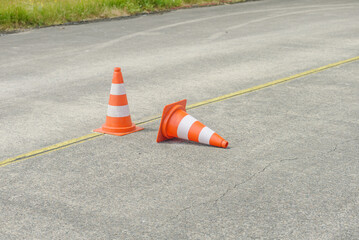 Two orange traffic cones on a paved road, one upright and one tipped over with a yellow line...