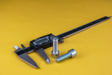 Digital vernier caliper and bolts on yellow background. Universal tool for high-precision...