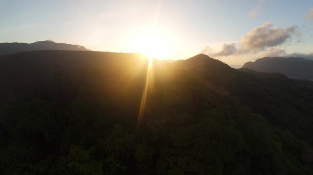 Drone ascends toward blazing sunrise as golden grass hills of Mount Tapyas merge with emerald forest and distant limestone peaks above Coron Bay in Palawan.