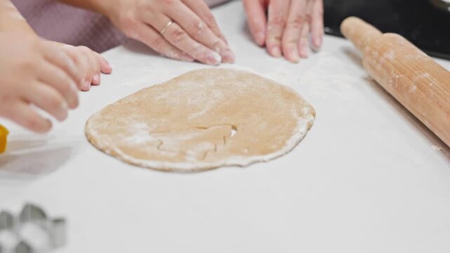 A child and their mom work together to shape cookies from gingerbread dough using festive cookie cutters. A heartwarming moment of family bonding during holiday preparations.