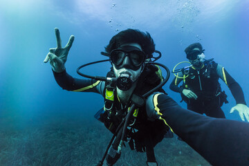 Two friends practicing scuba diving taking selfie, enjoying vacations adventure deep in the ocean