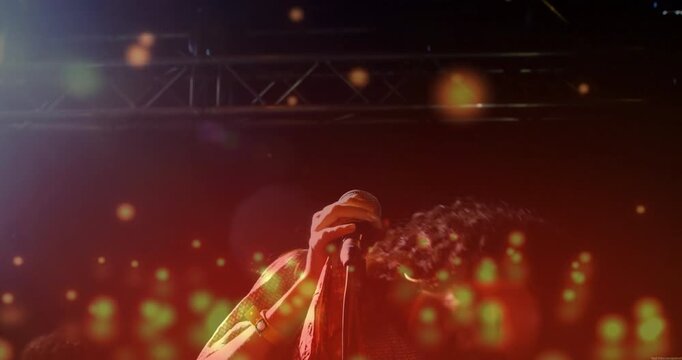 Spotlights lighting singer gripping microphone and performing music with gold bokeh lights drifting