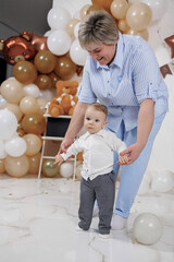 Grandmother helps toddler take first steps at a joyful celebration indoors