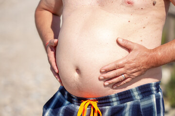 Big belly in a man. Close-up front view of a male body, shirtless, big belly, bloating, arms pressed to the body, belly button. Obesity, poor nutrition.