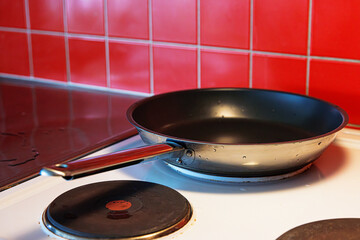 Coseup of a freshly washed clean teflon pan placed on a black cooking plate of a white electric stove with red tile backsplash.
