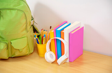 School books, headphones and backpack on a desk in a classroom during a break between lessons or...