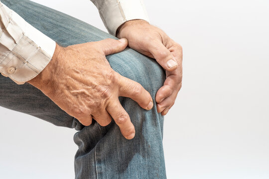 Arthritis symptoms, suffering from pain. The hands of the senior man massage a painful, inflamed male knee. Old age, health. Close up view..