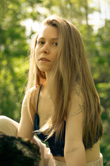 Naklejka premium Young woman with long hair sitting in forest, looking directly at camera.