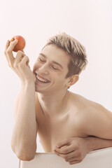 Cheerful Young Man Holding A Peach And Smiling In Bright Minimalist Portrait 