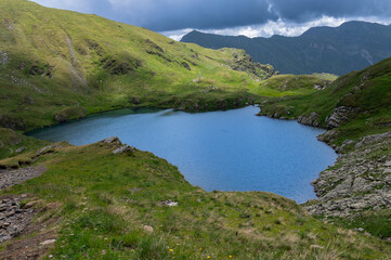 Capra Lake surrounded by mountains and green hills. Scenic summer view in the Fagaras Mountains, Romania.