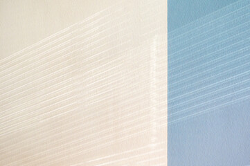 Soft sunlight casts striped shadows across a textured wall in pastel tones, evoking the feeling of sea and sand
