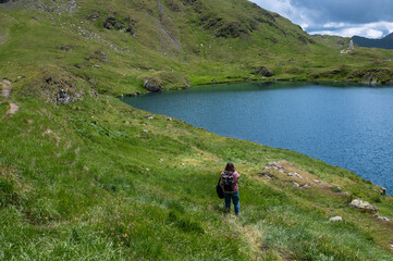 Person walking near Capra Lake in the Fagaras Mountains, Romania. Hiking in alpine nature with mountains and water.