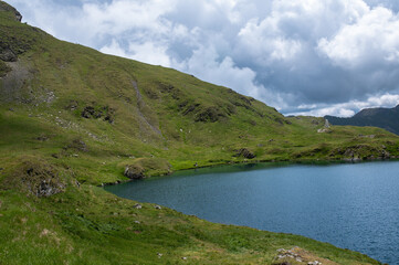 Capra Lake surrounded by mountains and green hills. Scenic summer view in the Fagaras Mountains, Romania.