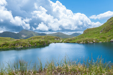Capra Lake in the Fagaras Mountains during summer. Cloudy weather over the alpine lake and green slopes of the Southern Carpathians in Romania. Outdoor adventure and scenic Transylvanian landscape.