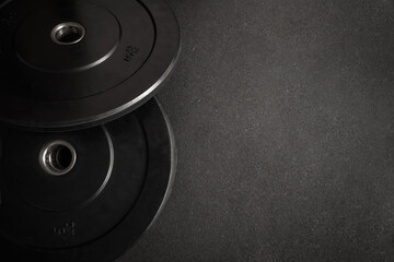Black bumper plates sit on a dark gym floor, creating a simple yet powerful image of strength training and fitness. Empty space for text