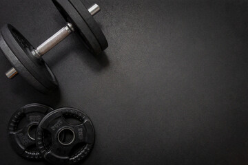 Black dumbbell and weights lying on a dark gym floor, creating a fitness-focused composition with ample copy space
