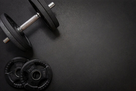 Black dumbbell and weights lying on a dark gym floor, creating a fitness-focused composition with ample copy space