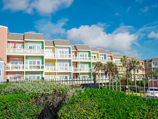 Enclosed by metal fencing over beachfront pastel townhomes open balconies. Palm trees and lush landscaping enhance the Gulf Coast setting and secure vacation rental appeal, upscale rental units