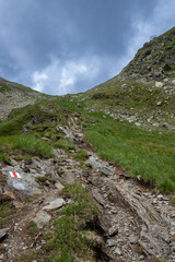 Rocky mountain trail with patches of grass under a blue sky. Hiking path in the Făgăraș Mountains, Transfăgărășan, Romania.