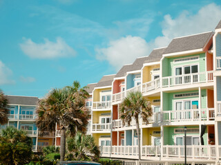 Intersecting rows of colorful beach condos townhomes with tall palm trees under sunny cloud blue...