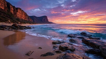 Gentle waves washing onto a pristine sandy beach at sunrise, with dramatic cliffs and a vibrant sky creating a breathtaking coastal landscape in royal national park, australia