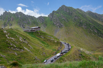 Mountain road transfagarash in the Fagaras Mountains, Romania, with a line of cars and a small alpine cabin surrounded by dramatic peaks