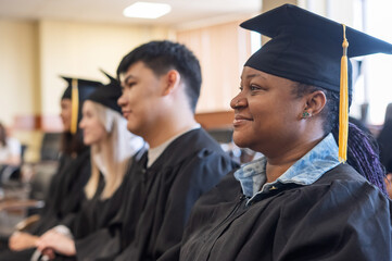 Young people in graduation gowns listen to a speech by a classmate. 