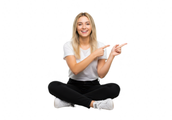A happy young woman in casual clothes sits crosslegged and points in two directions, isolated on a transparent background