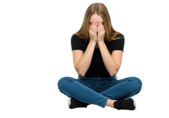 A distressed young woman sitting crosslegged in jeans and a tshirt, hiding her face in her hands, isolated on white isolated on transparent background
