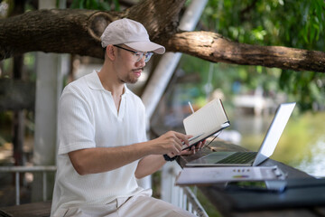 man is sitting on a bench with a laptop and a notebook