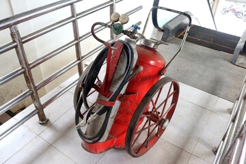 A detailed photo of an old red fire extinguisher on wheels, equipped with hoses, gauges, and metal...