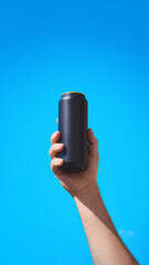 Black drink can held in hand for mockup with blue sky background for beverage branding. Concept of...