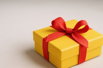 Obraz premium Bright yellow gift box with red ribbon bow on plain neutral background.