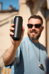 Matte black drink can held by smiling man in sunglasses under sunlight. Concept of beverage...