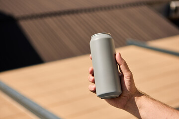 Matte grey drink can held in male hand with rooftop in soft background light. Concept of beverage...