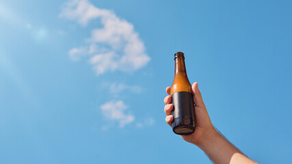 Beer bottle with blank label held against clear blue sky. Concept of packaging design, advertising,...