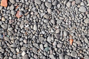 Gravel stone background for the construction industry. A close-up photo of texture of gray rocks with some that are orange in color.
