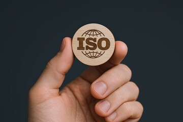 Close-up of a hand holding a round wooden ISO certification token with globe design.