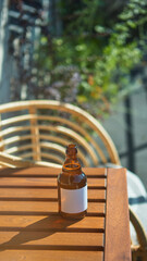 Amber glass bottle featuring unmarked label on wooden surface in sunlit outdoor environment....