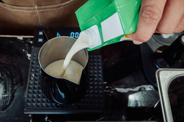 Barista pouring milk into a coffee drink placed on a digital scale to measure precise ratio for...
