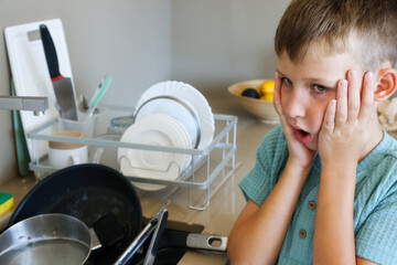 Shocked Boy Looks at Dirty Dishes in Kitchen Sink