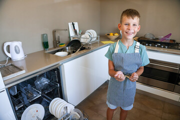 Happy Boy in Apron Standing in Kitchen with Dirty Dishes