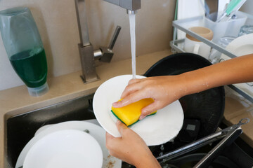 Close-Up of Hands Washing Plate Under Running Water with Sponge in Kitchen Sink