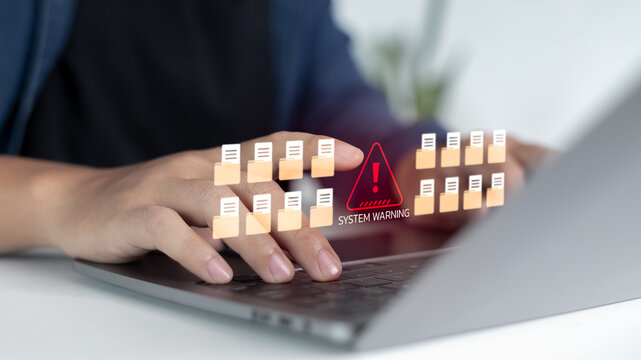 Close-up hands typing laptop with warning alert icon and many file folders, concept of data breach, system error, information leak, cybersecurity protection.
