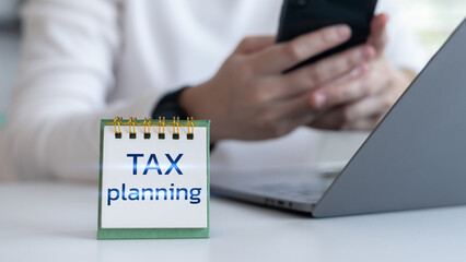 Mini calendar with Tax Planning text on desk, person using smartphone and laptop, financial planning, tax filing preparation, accounting concept.