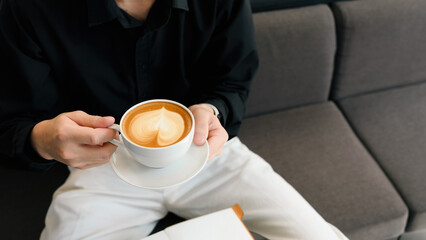 Peaceful break time with a close-up image of a man in black shirt holds latte with latte art in cafe