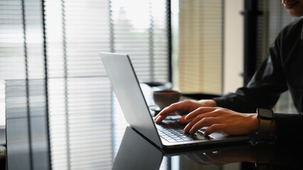 Close-up of man’s hands typing on a laptop in a bright office with coffee nearby